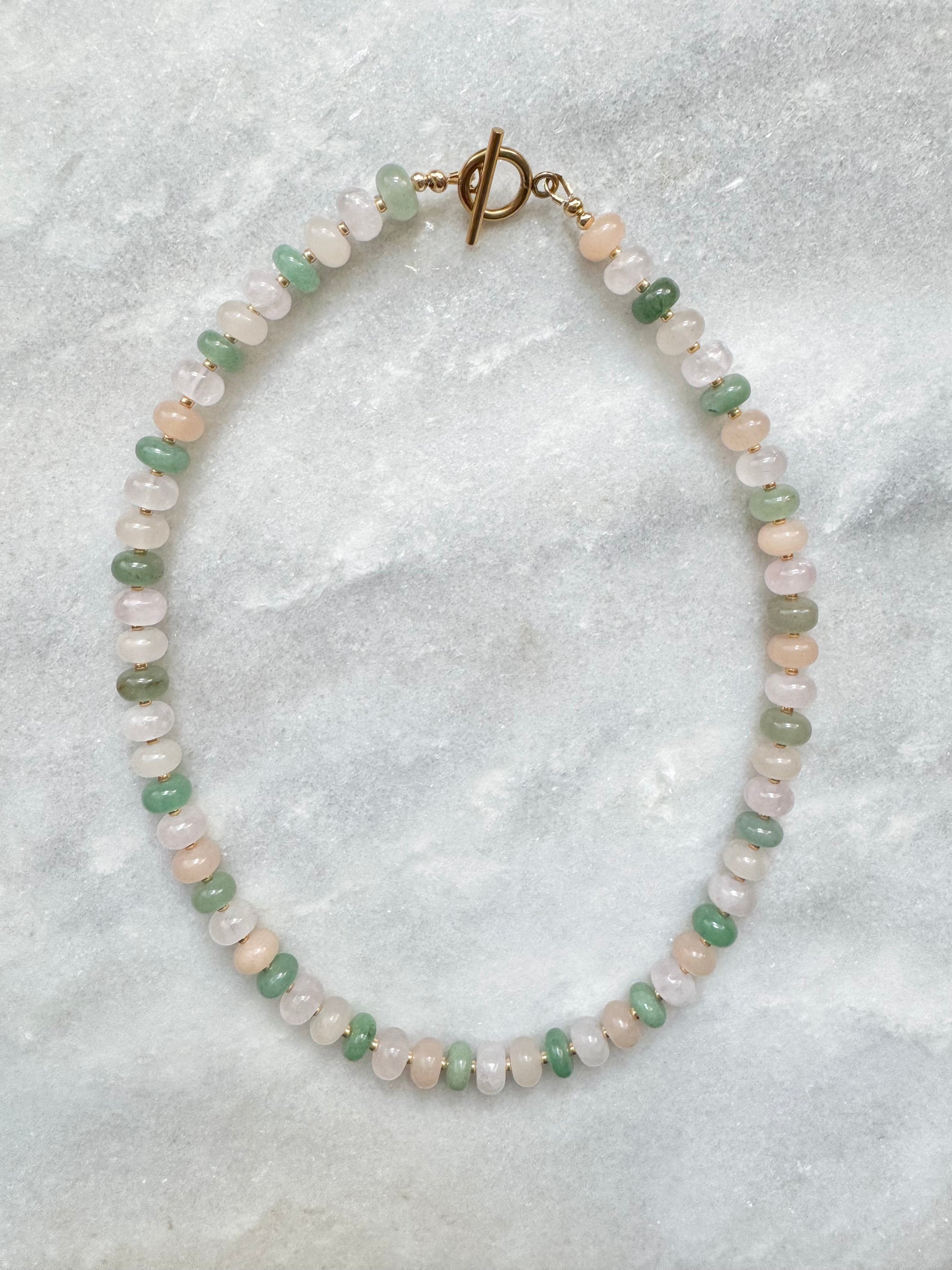 Necklace with green and pink beads on a textured gray background