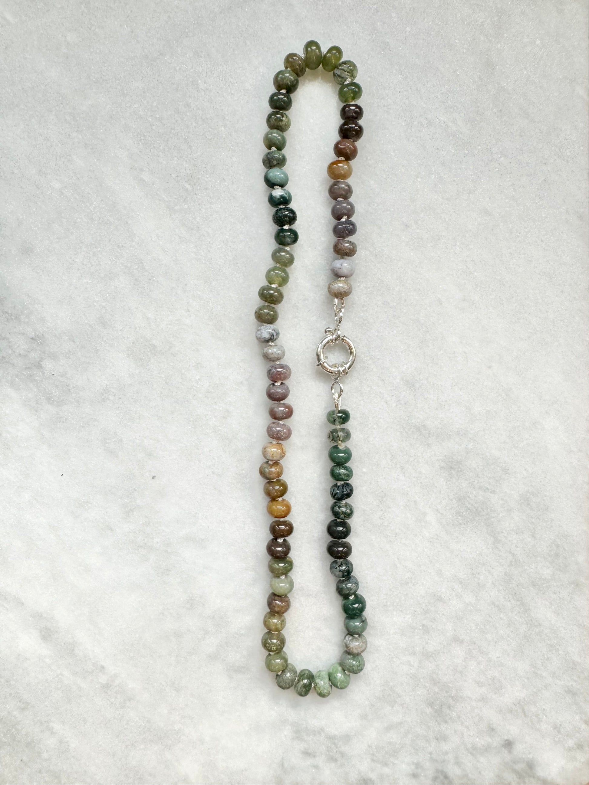 hand knotted necklace with a silver clasp on a textured white background