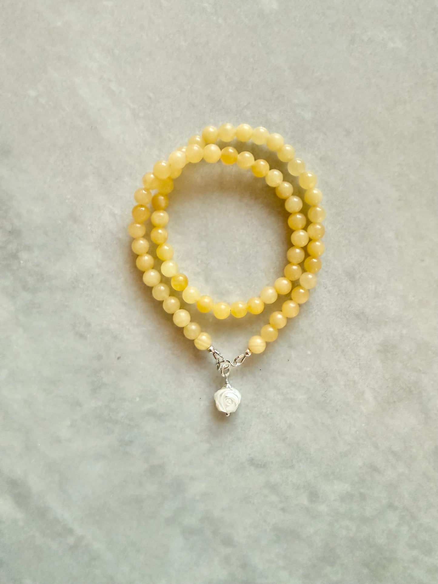 Beaded made of yellow gemstone beads with a small sterling silver clasp and rose charm, displayed on a light gray textured surface.