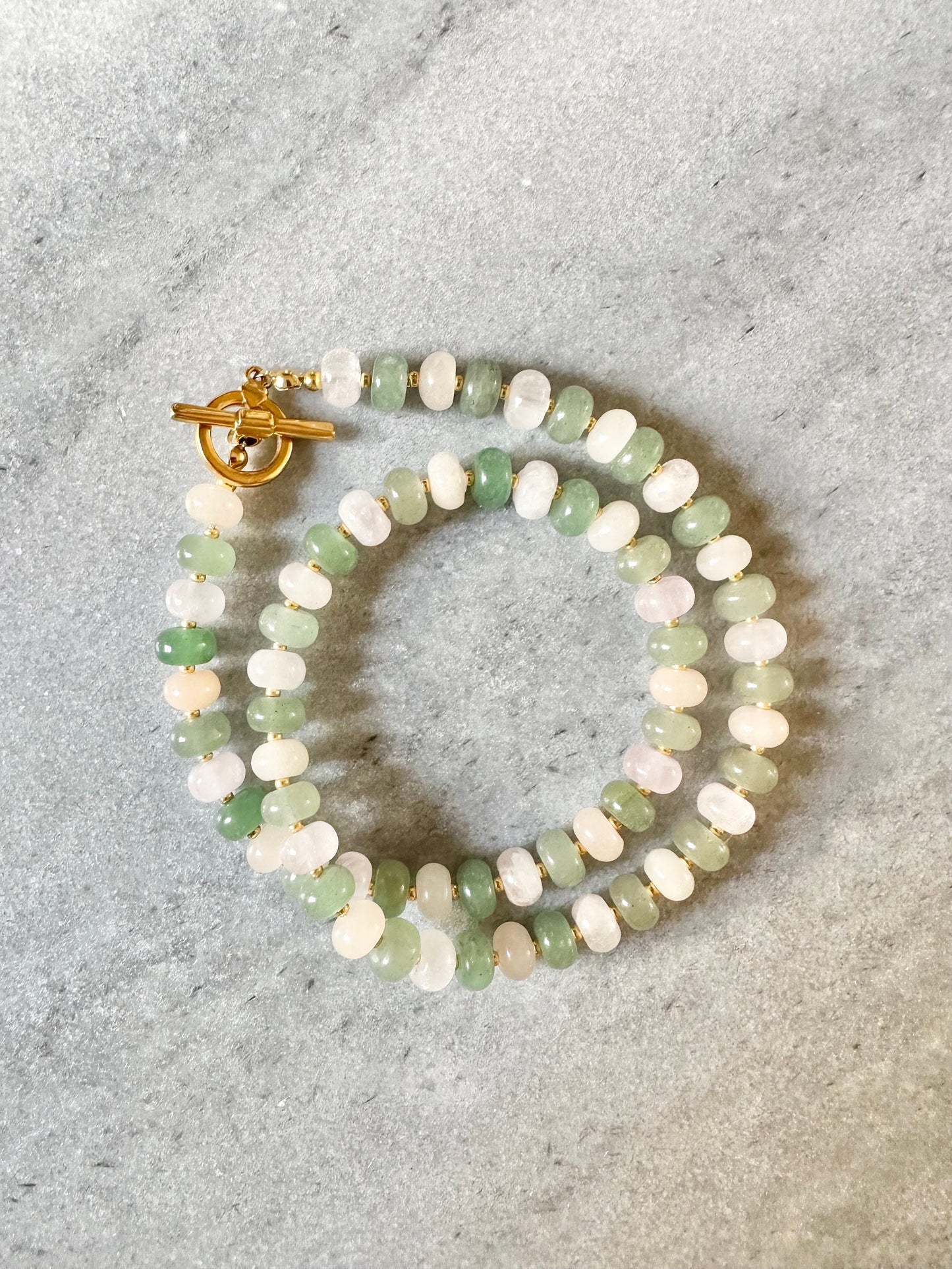 A beaded necklace with a green and pink aventurine and rose quartz design, featuring a gold plated toggle clasp.