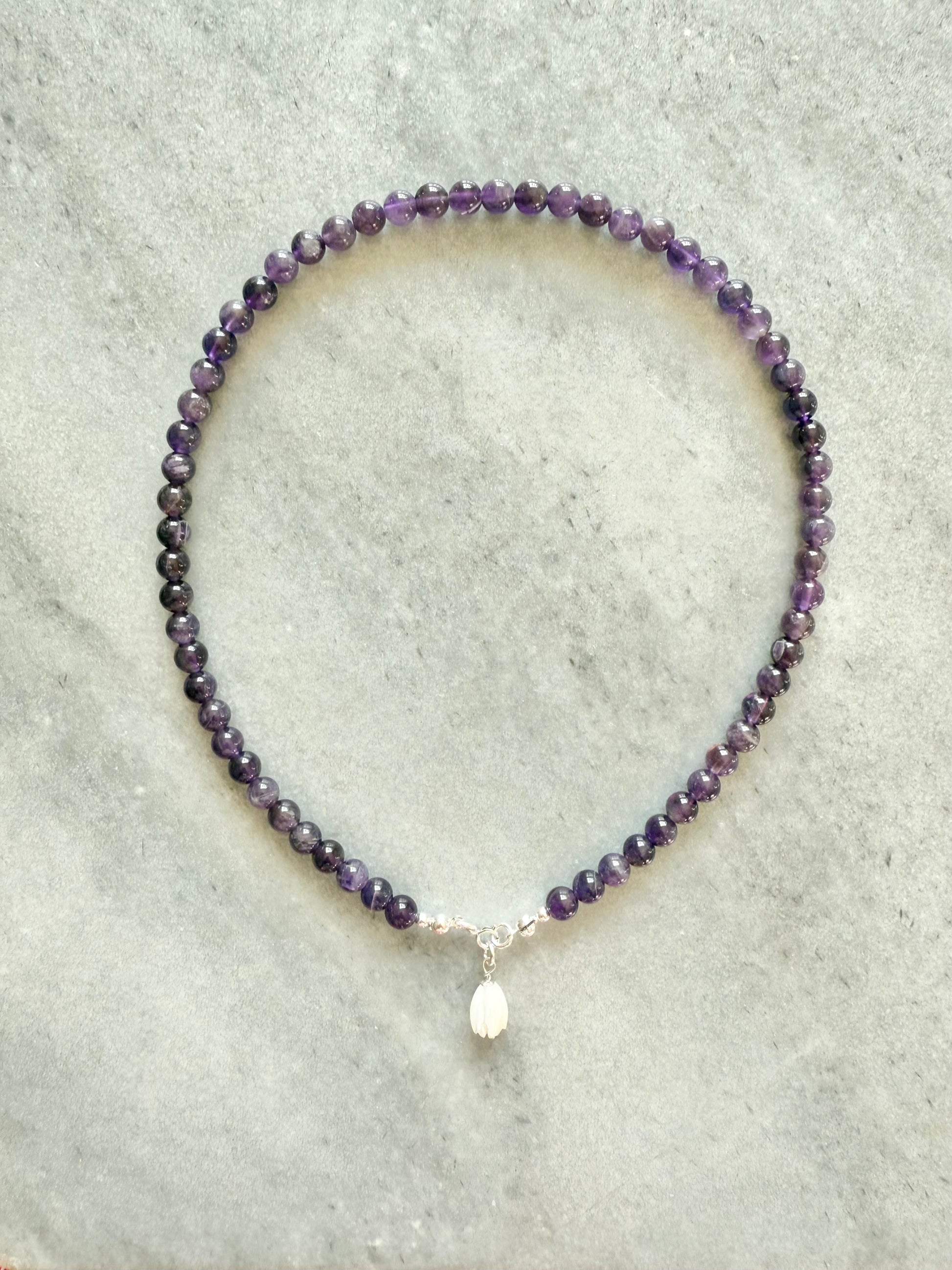 Purple beaded necklace with a silver clasp on a light gray background