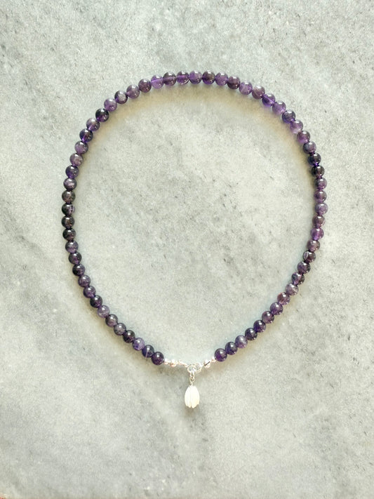 Purple beaded necklace with a silver clasp on a light gray background