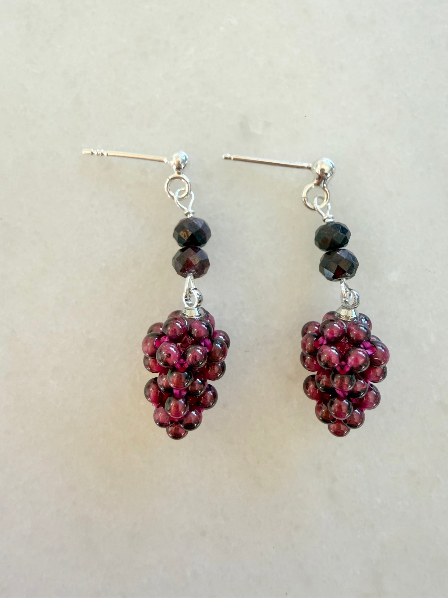 Pair of earrings with purple bead clusters on a light gray background