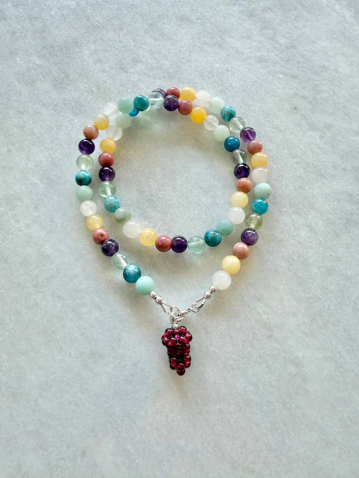 A beaded necklace featuring multicolour gemstone beads and a dangling dark red garnet cluster charm.