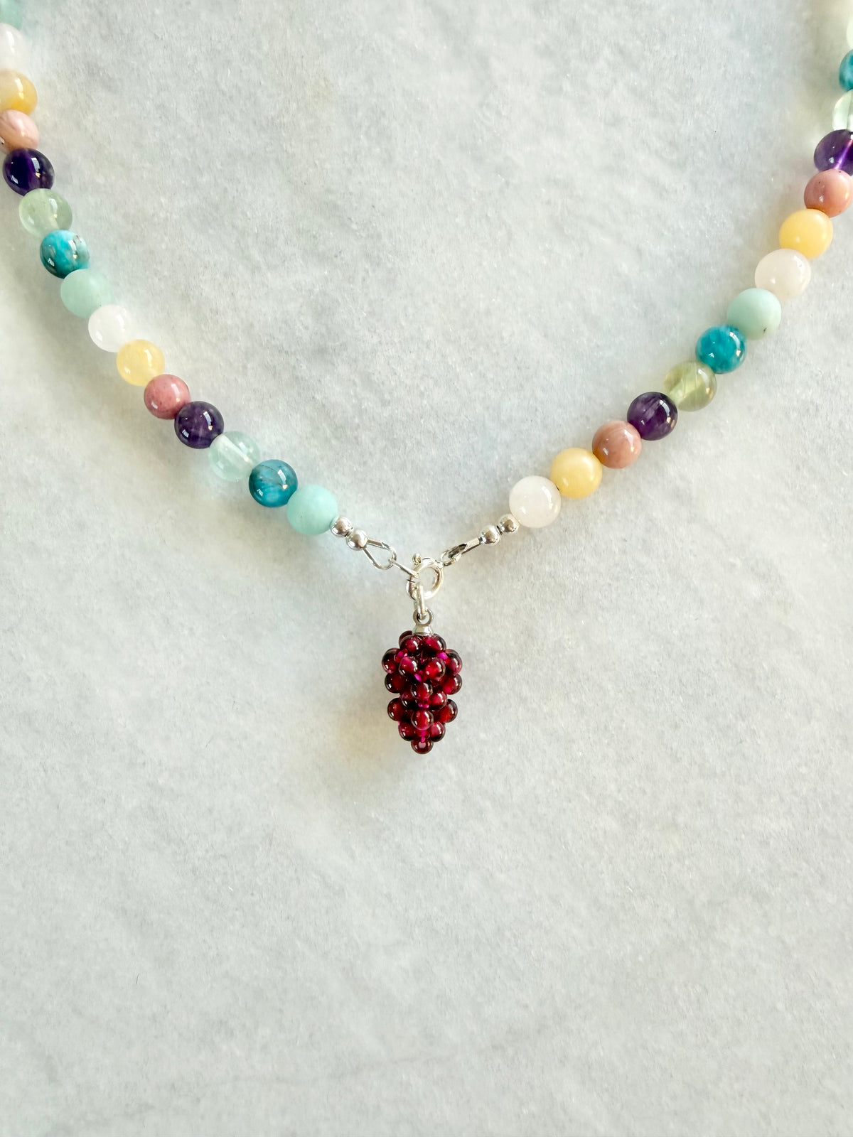 Necklace with multicolored beads and a red berry pendant on a light gray background