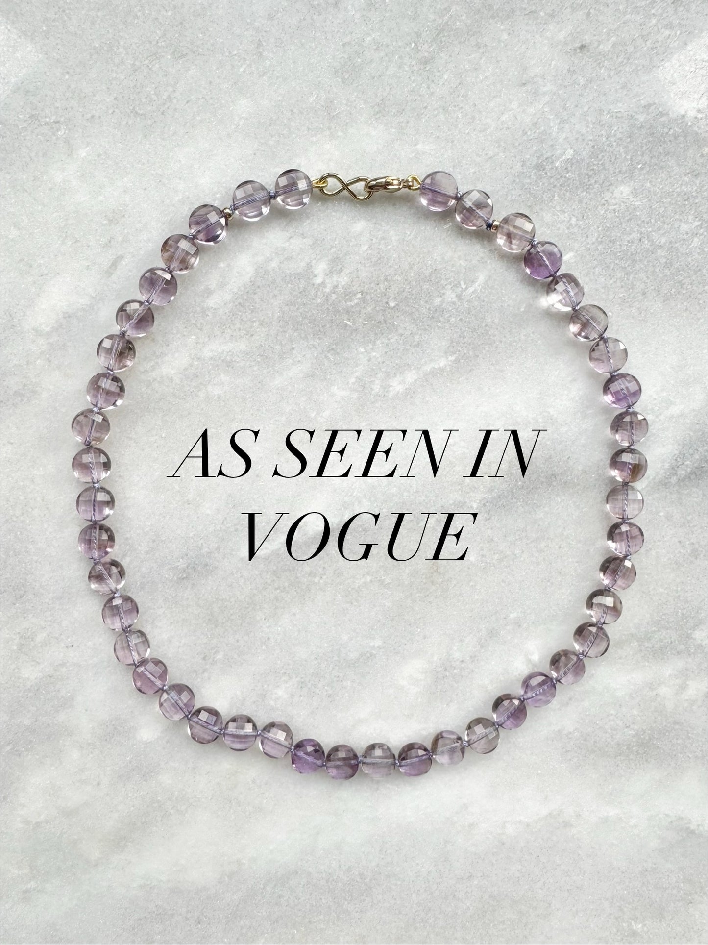 Purple beaded necklace on a textured gray background with 'As Seen in Vogue' text.