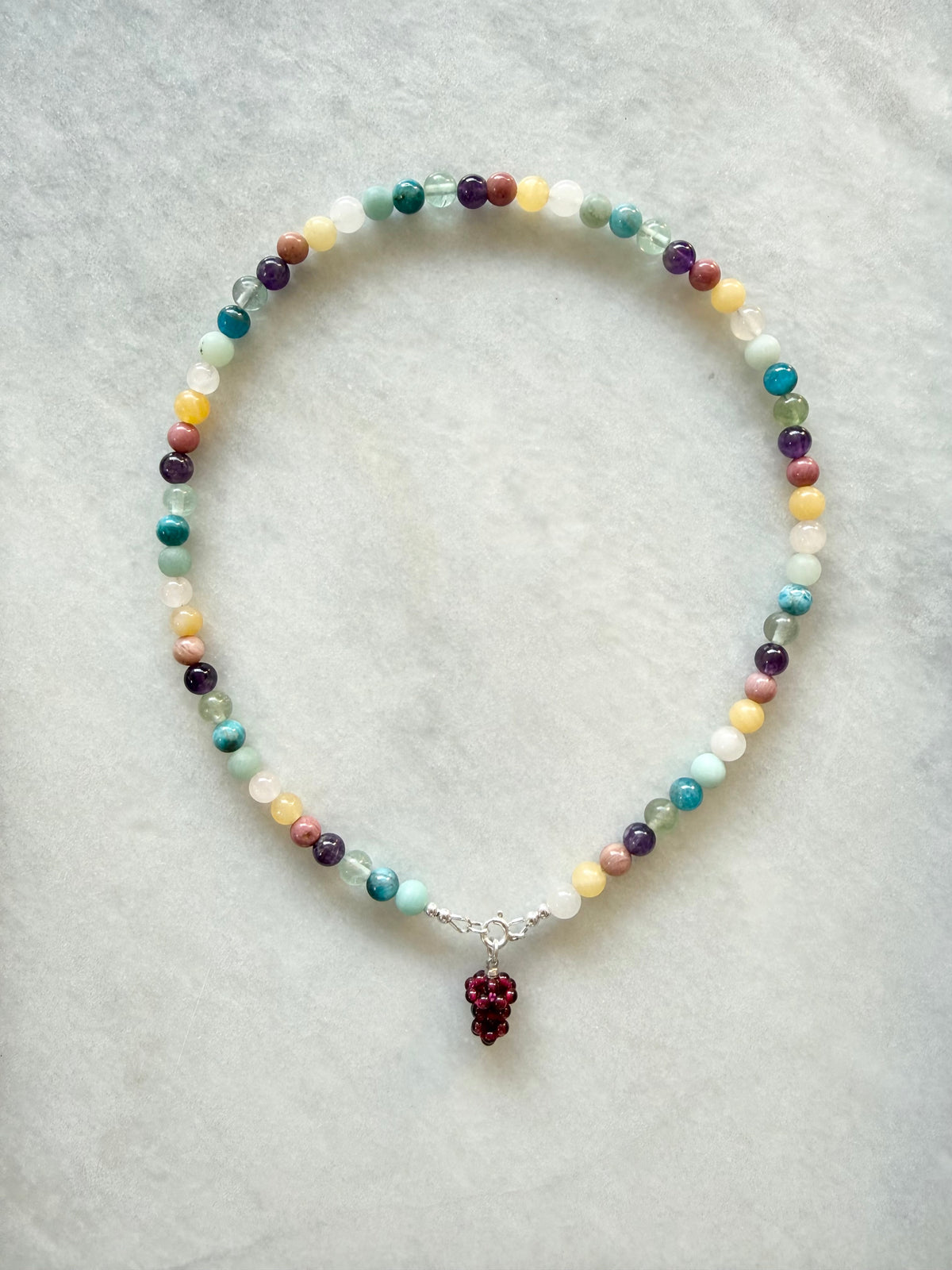 Multicolored beaded necklace with a grape-shaped pendant on a light gray background