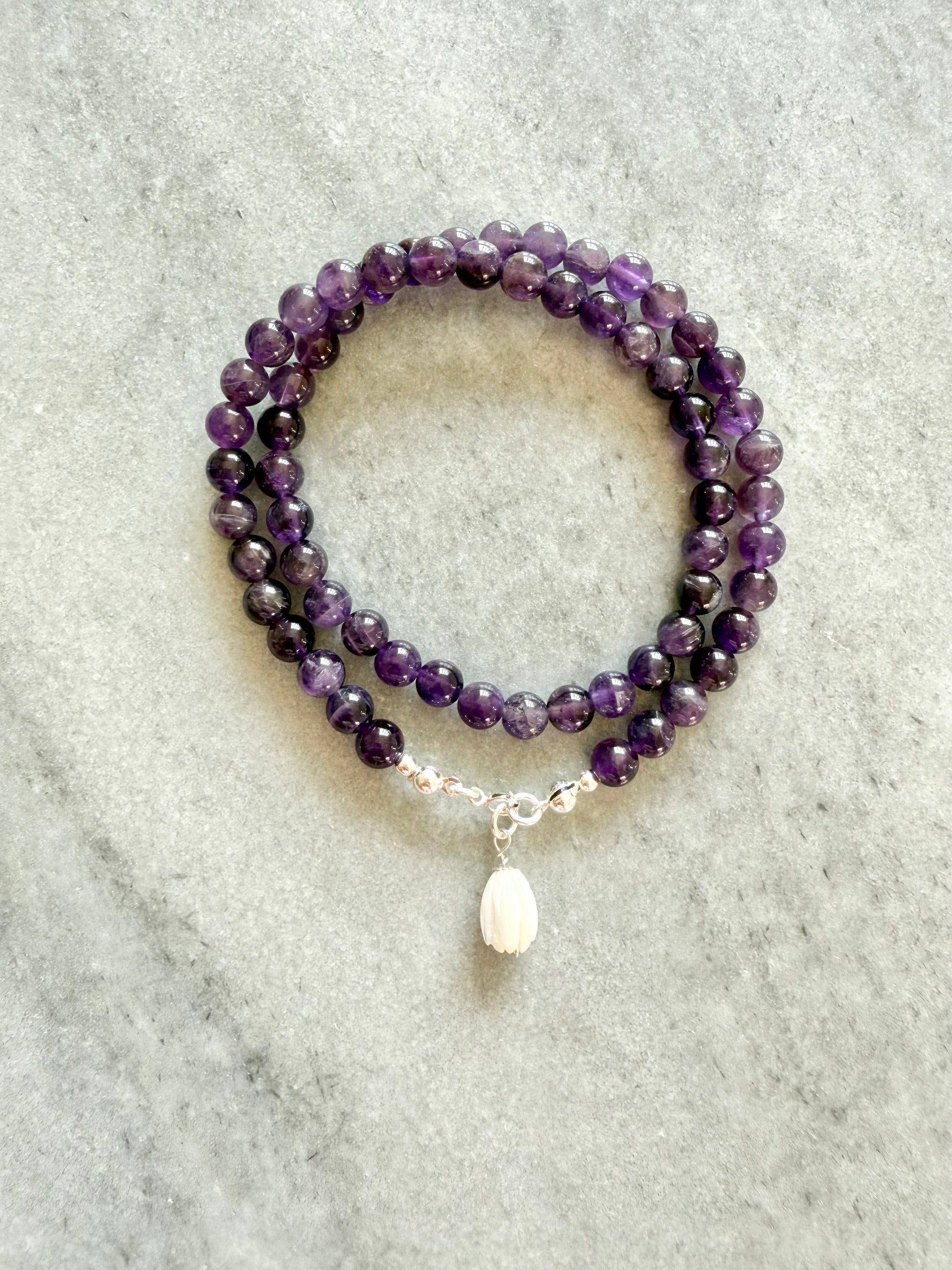 Amethyst beaded bracelet with a silver charm on a light gray surface