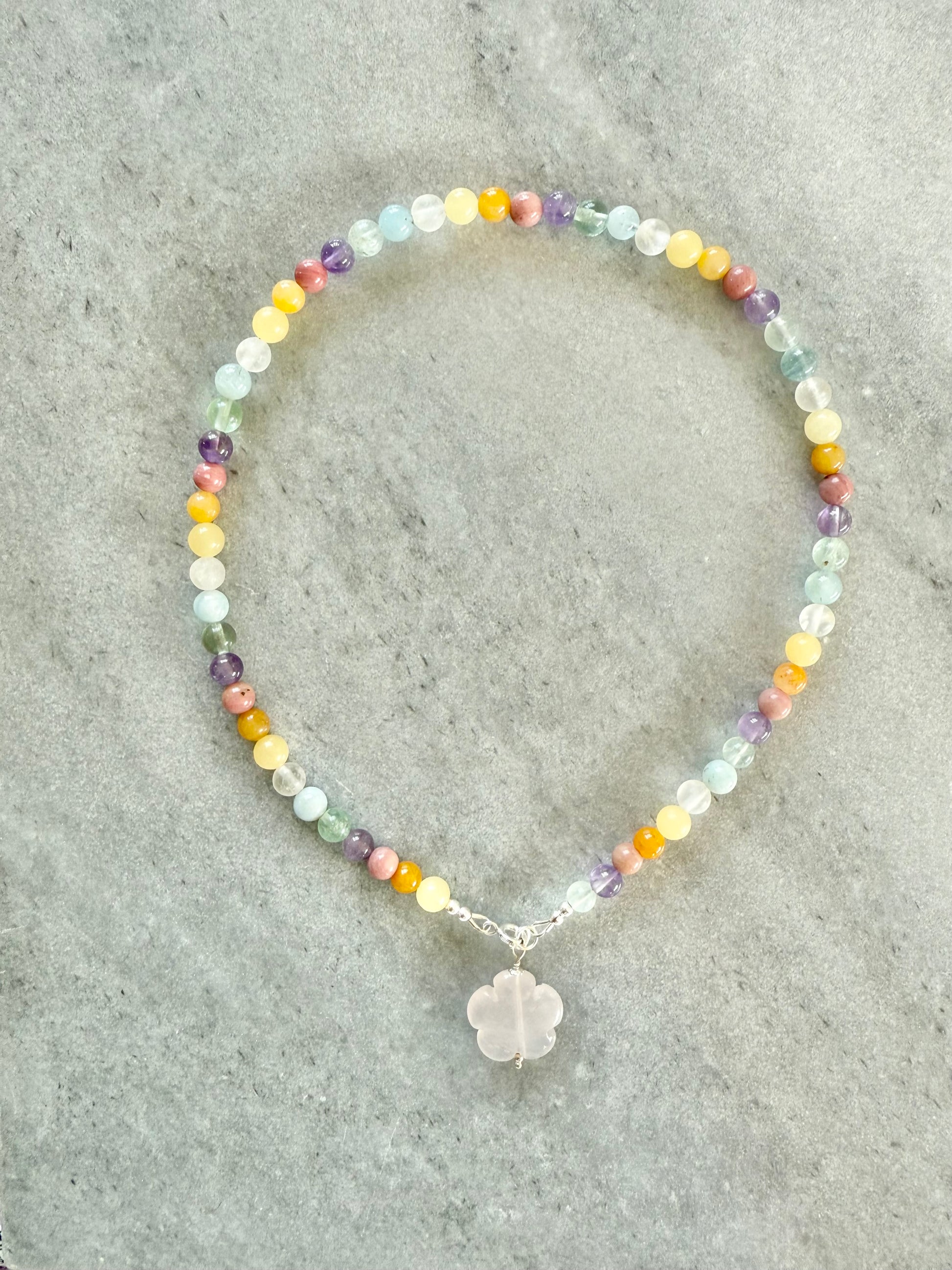 Multicolored beaded necklace with a silver charm on a gray surface