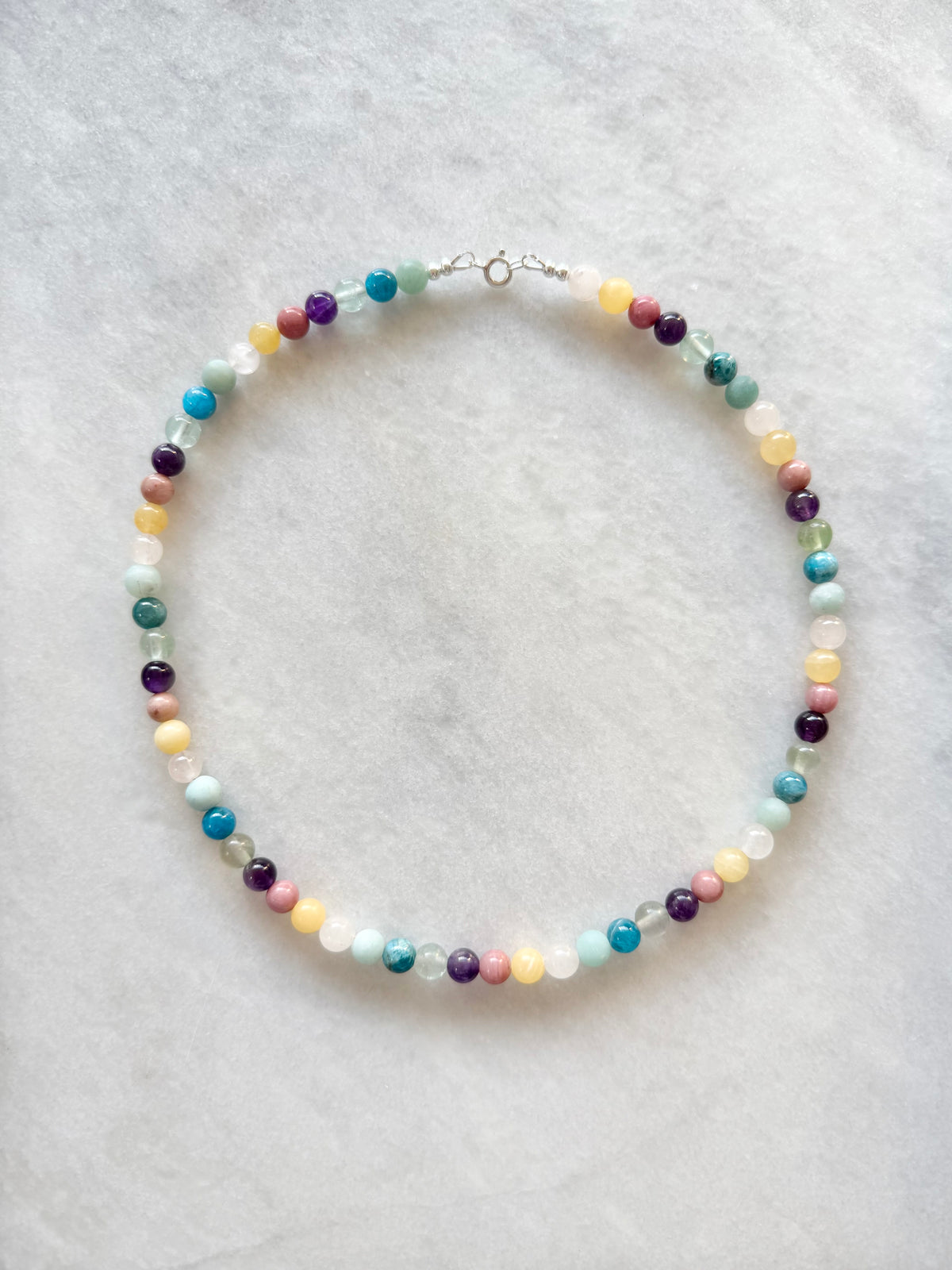 A beaded necklace made of small multicoloured gemstone beads in pastel and earthy tones.
