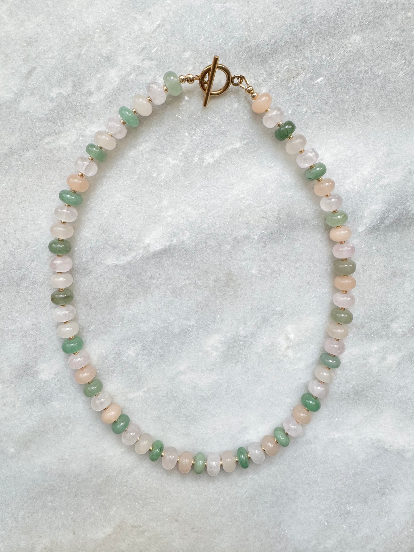 Necklace with green and pink beads on a textured gray background