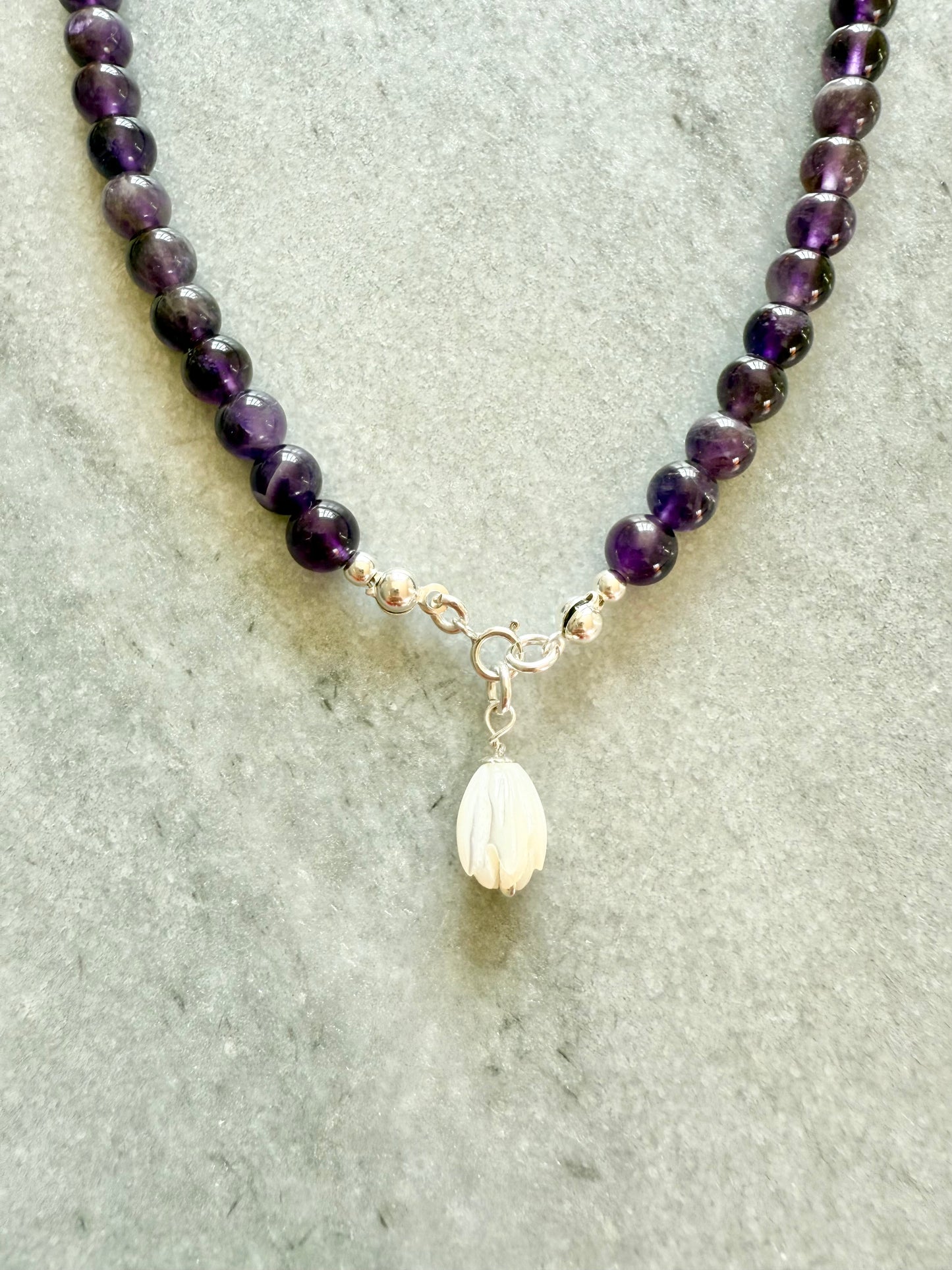 Necklace with purple beads and a white pendant on a gray surface