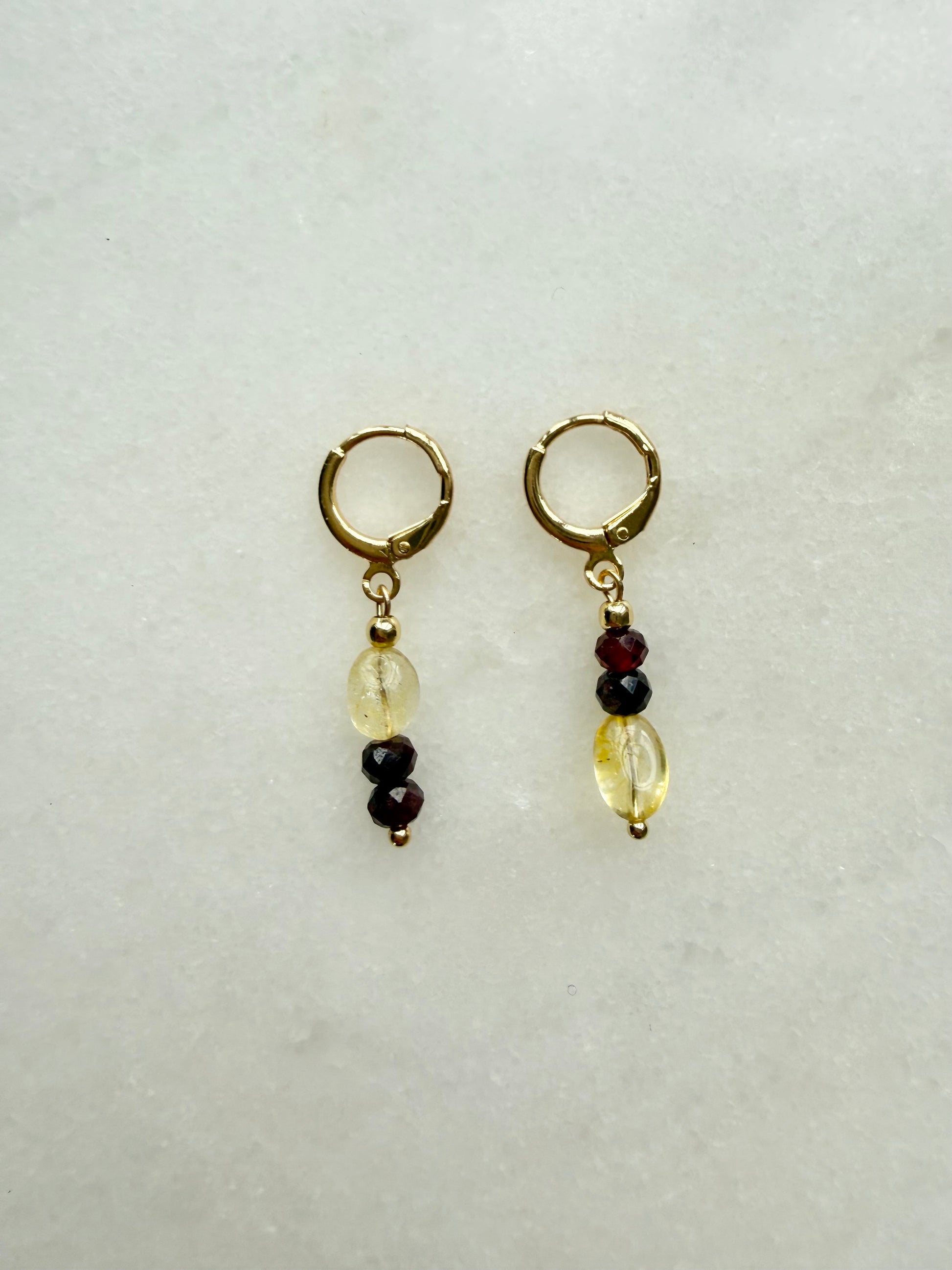 Pair of gold hoop earrings with beaded charms on a light gray background