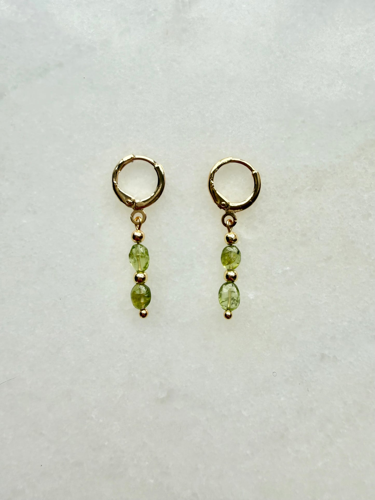 Pair of gold earrings with green beads on a white background