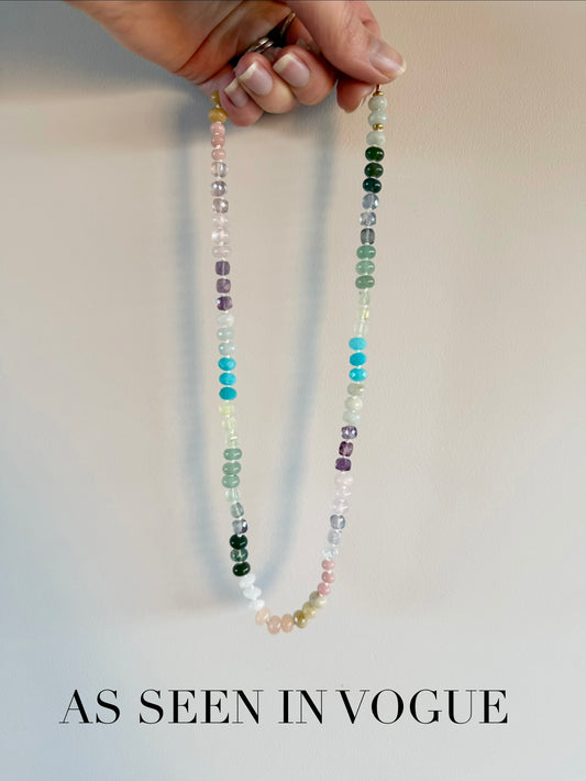 Multicolored beaded necklace held by a hand against a plain background with 'As Seen in Vogue' text.