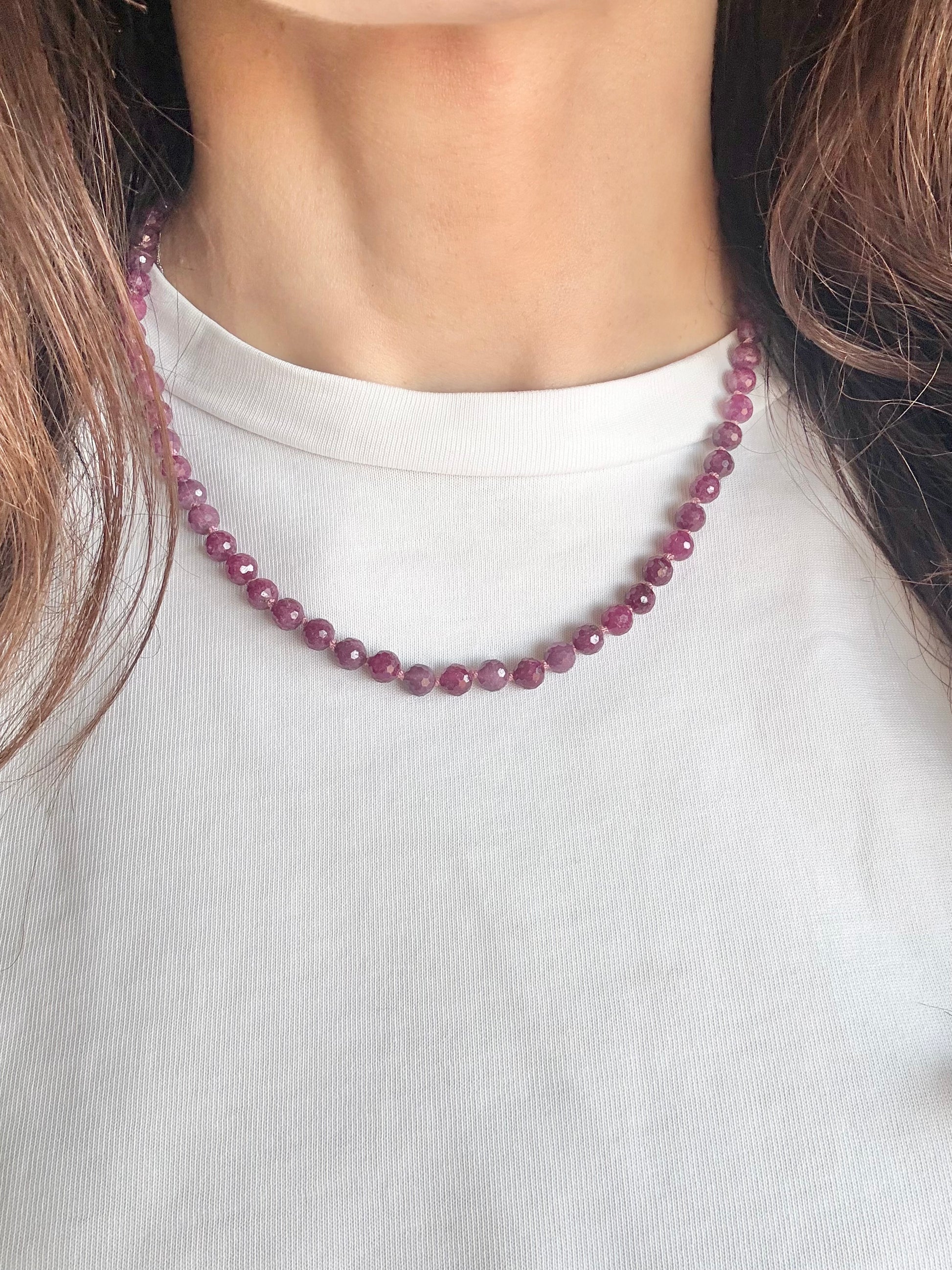 Person wearing ahand knotted ruby necklace on a plain white background
