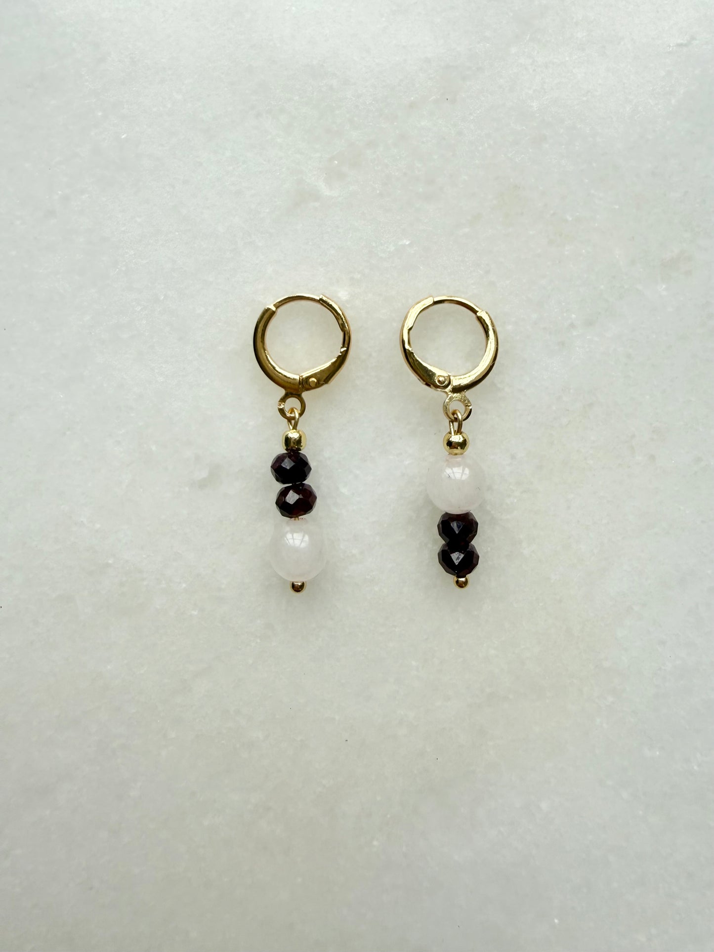 Pair of gold hoop earrings with black and white bead drops on a light gray background
