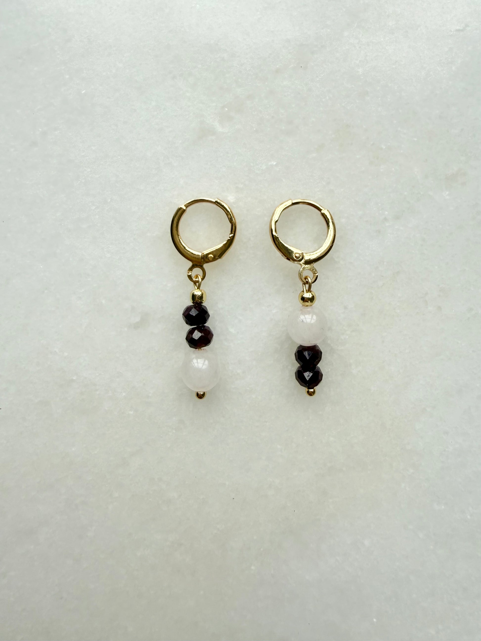 Pair of gold hoop earrings with black and white bead drops on a light gray background