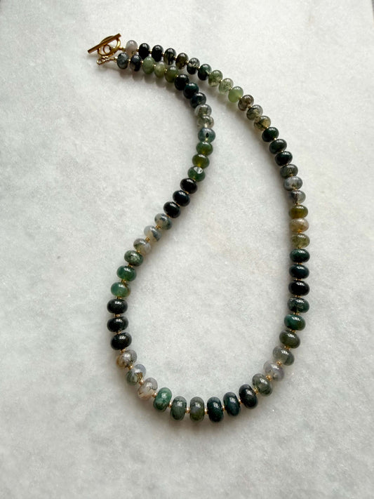 Necklace with green and black beaded chain on a white background