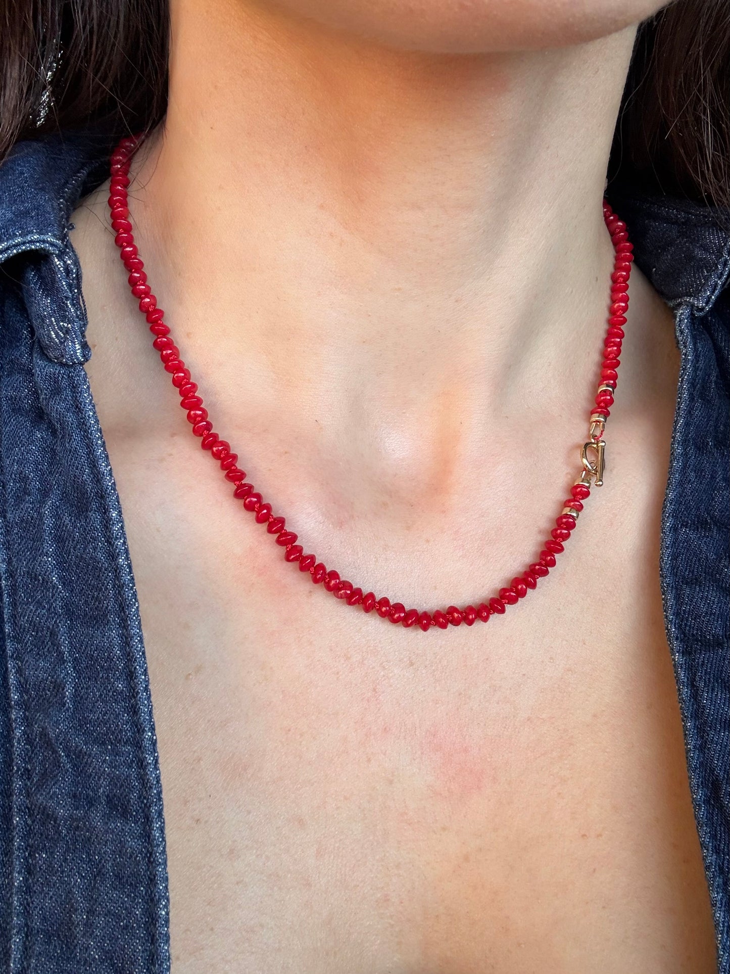 Red beaded necklace on a person wearing a blue denim shirt.