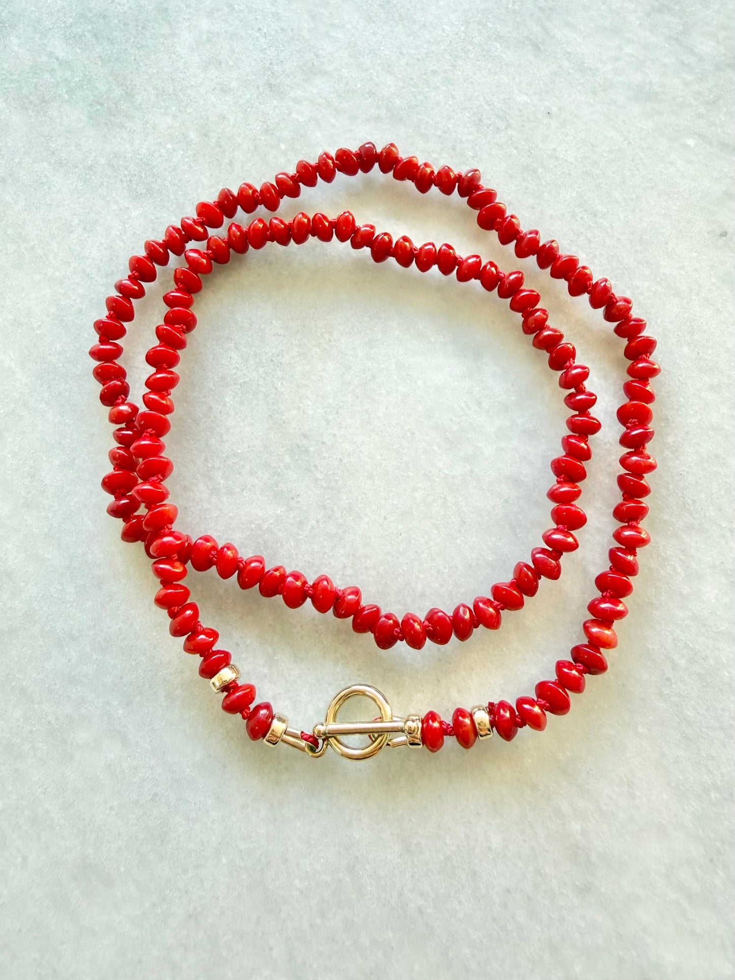 Red beaded necklace with a gold clasp on a light gray background
