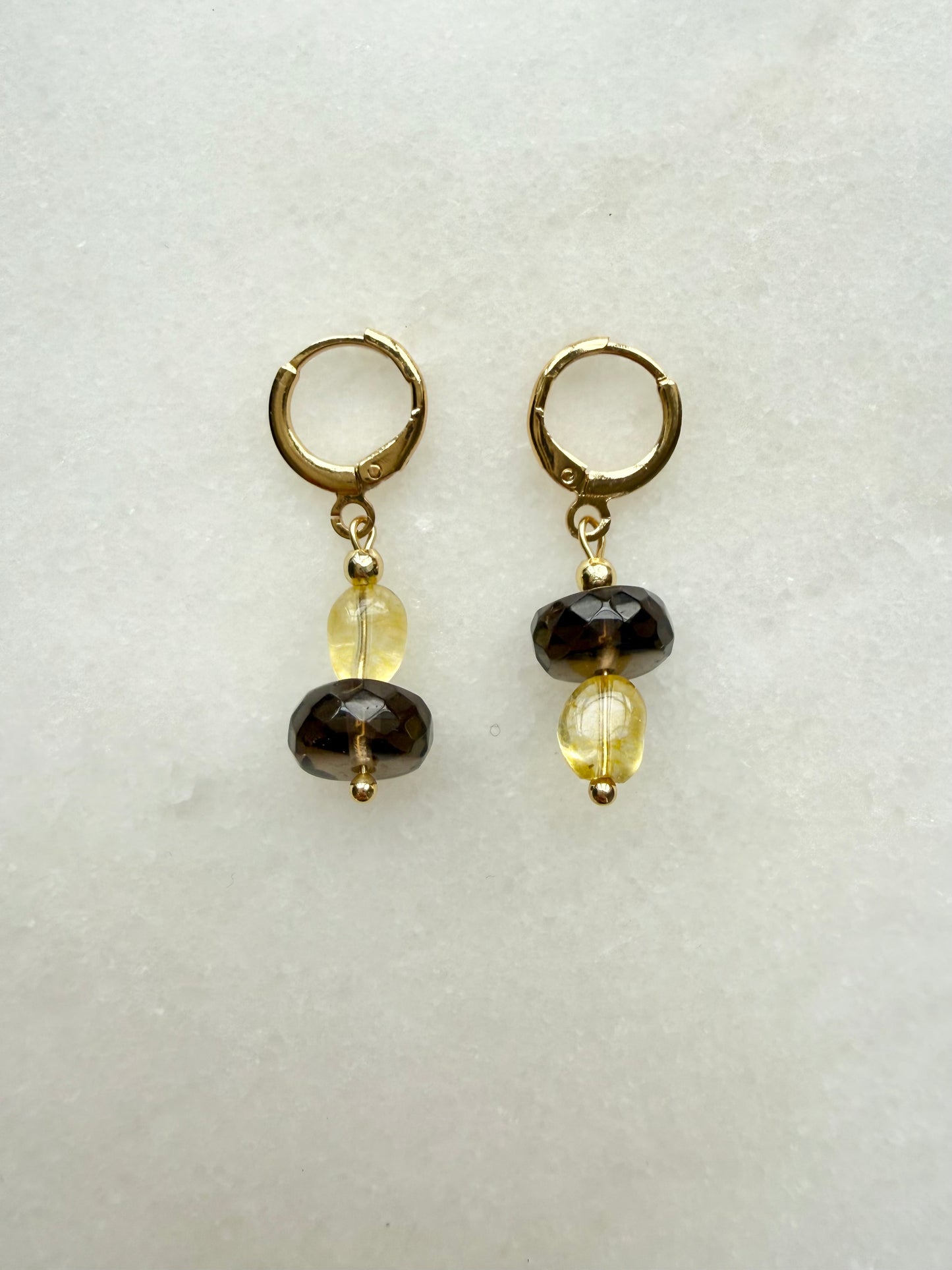 Pair of earrings with gold hooks, black and yellow beads on a light gray background