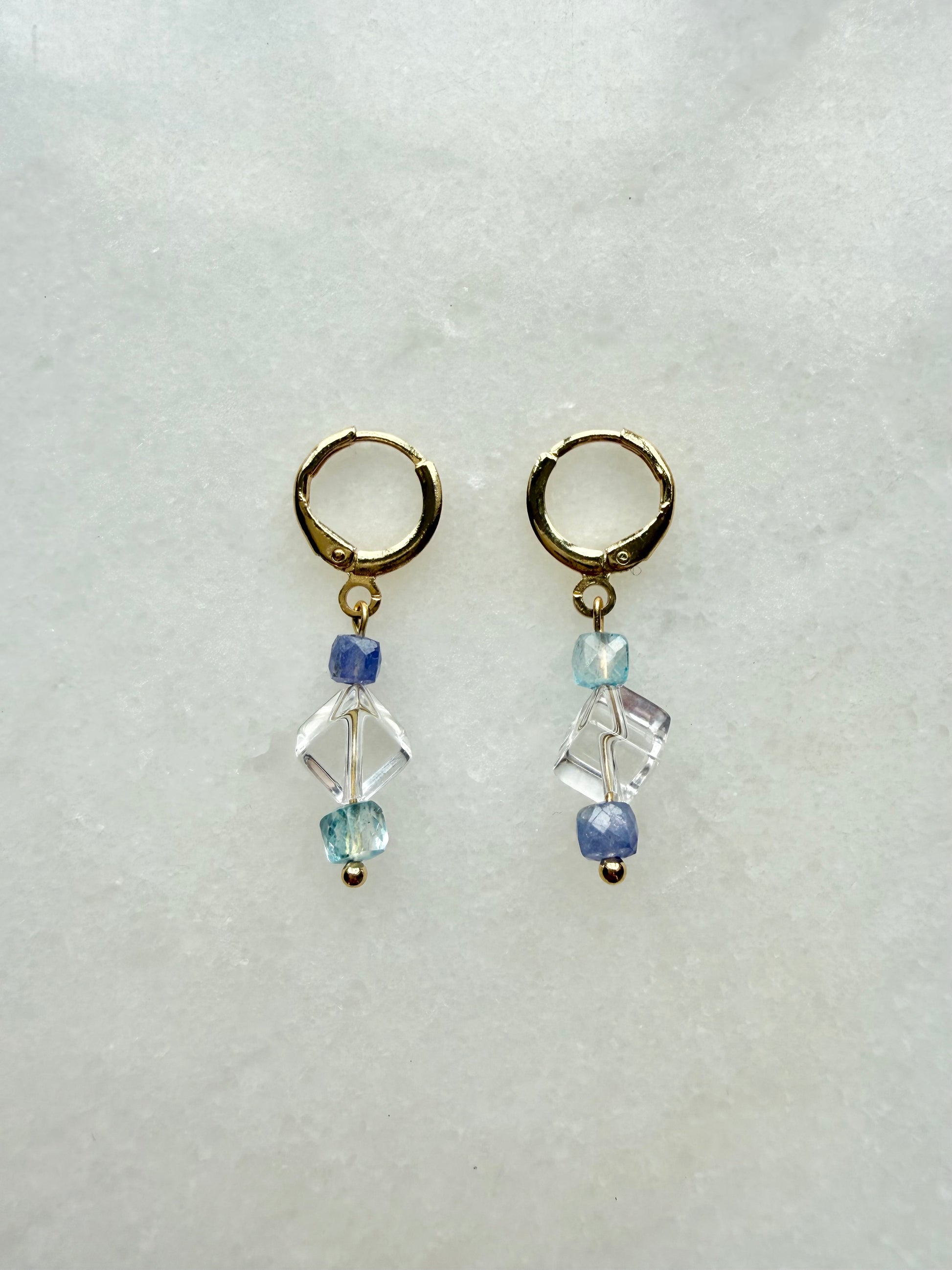 Pair of gold hoop earrings with blue and clear bead drops on a light gray background