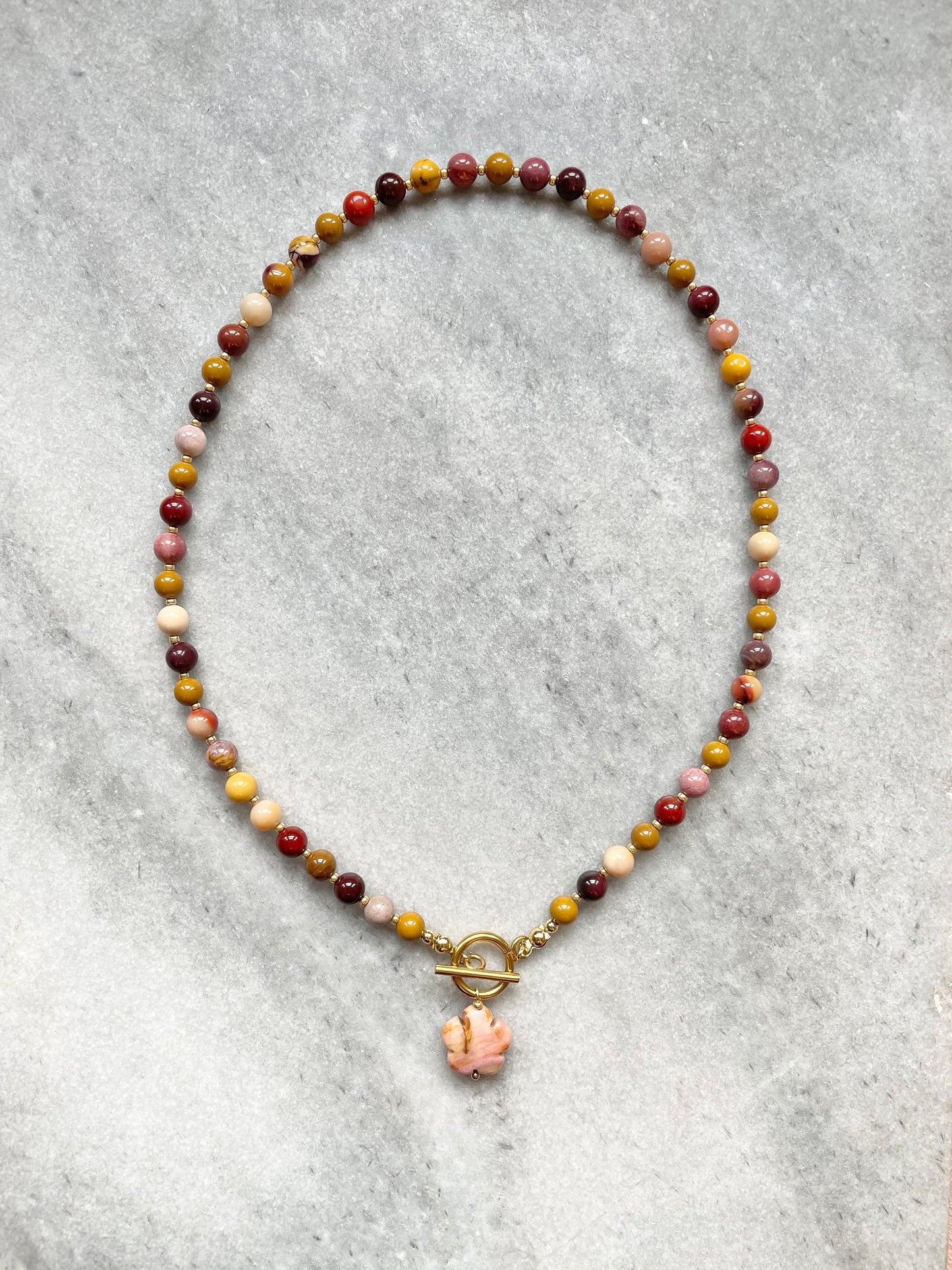 A beaded necklace with a flower pendant, featuring mookaite jasper beads and gold seed beads, with a gold-filled stainless steel clasp.