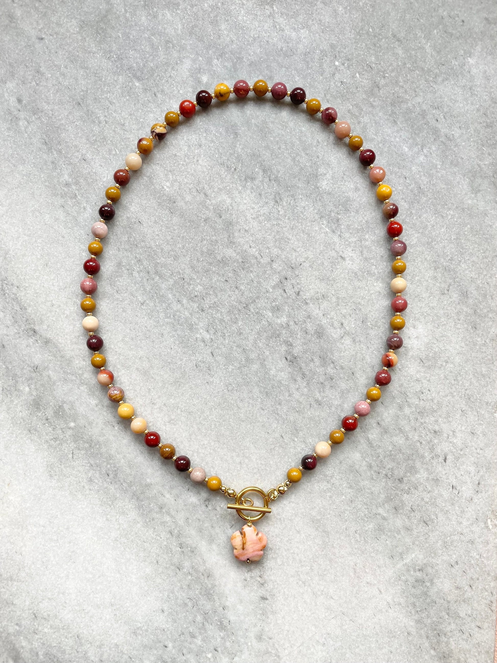 A beaded necklace with a flower pendant, featuring mookaite jasper beads and gold seed beads, with a gold-filled stainless steel clasp.